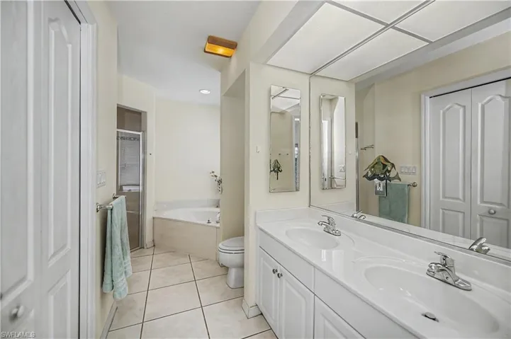 Bathroom featuring a double vanity with white cabinetry, a large mirrored wall, and a tiled floor