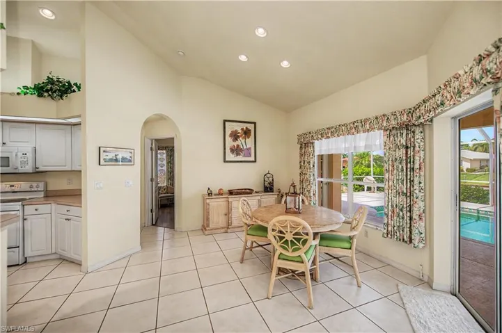 Open-concept dining area featuring vaulted ceilings, recessed lighting, tile flooring, an arched doorway, and a sliding glass door providing natural light and exterior access