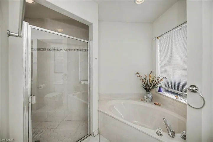 Bathroom featuring a built-in soaking tub, glass-enclosed shower, white tile flooring, and a window with blinds