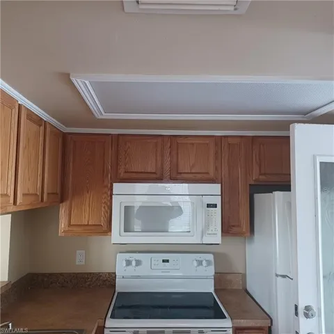 Kitchen with white appliances, brown cabinetry, and dark countertops