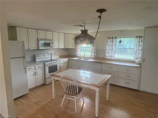 Kitchen featuring backsplash, white appliances, light hardwood / wood-style floors, and white cabinets