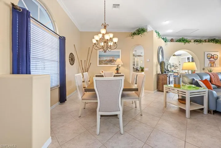 Dining area with ornamental molding, arched walkways, a chandelier, and light tile patterned flooring