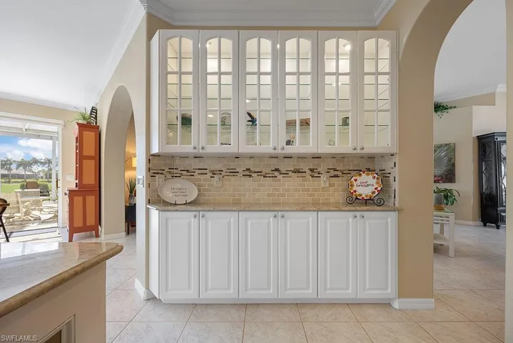 Kitchen featuring arched walkways, crown molding, light tile patterned flooring, glass insert cabinets, and decorative backsplash