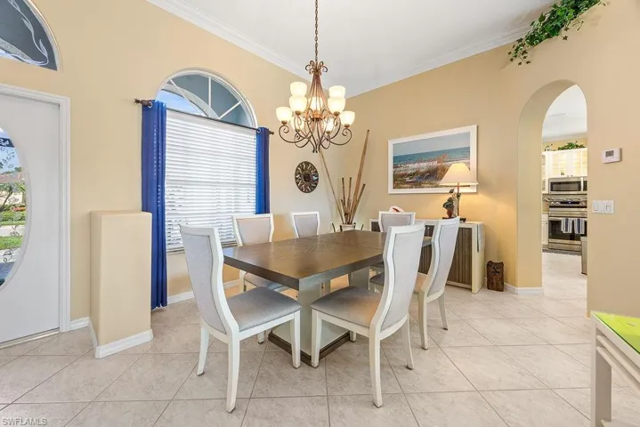 Dining room featuring crown molding, a chandelier, light tile patterned flooring, and arched walkways