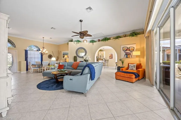 Living area with ceiling fan, ornamental molding, light tile patterned floors, arched walkways, and a chandelier