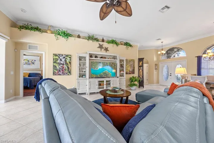 Living area featuring a chandelier, ceiling fan, light tile patterned flooring, ornamental molding, and arched walkways