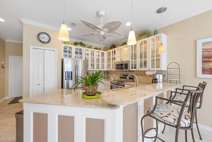 Kitchen with stainless steel appliances, ornamental molding, a peninsula, light stone counters, and backsplash