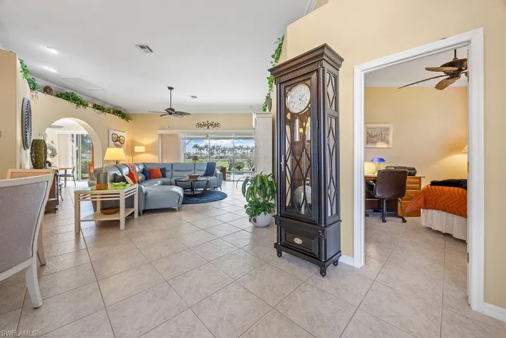 Living room featuring ceiling fan, light tile patterned floors, arched walkways, and a desk
