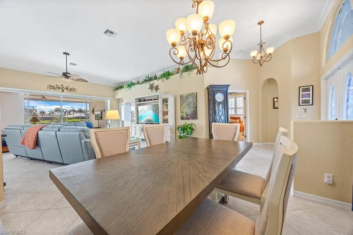 Dining room with light tile patterned floors, arched walkways, a chandelier, ceiling fan, and ornamental molding