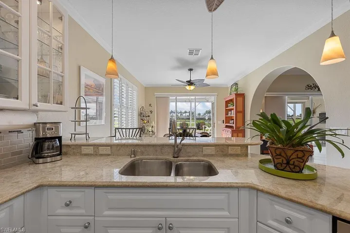 Kitchen with crown molding, glass insert cabinets, white cabinets, and light stone counters
