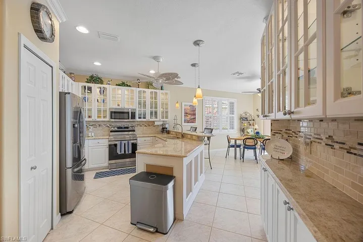 Kitchen with stainless steel appliances, decorative backsplash, a peninsula, ceiling fan, and light tile patterned floors