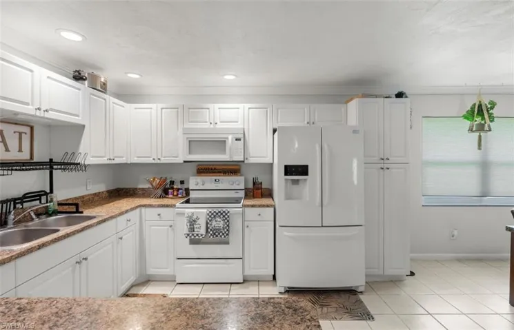 Kitchen with sink, light tile patterned flooring, white cabinets, and white appliances
