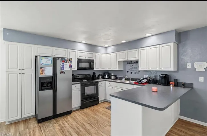 Kitchen with white cabinets, black appliances, light hardwood / wood-style flooring, and kitchen peninsula