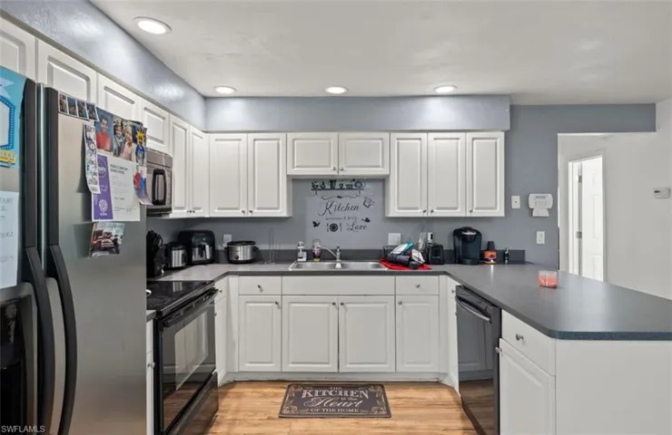 Kitchen featuring white cabinetry, kitchen peninsula, light hardwood / wood-style floors, black appliances, and sink