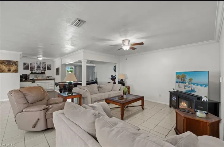 Living room featuring ornate columns, light tile patterned floors, ceiling fan, and crown molding
