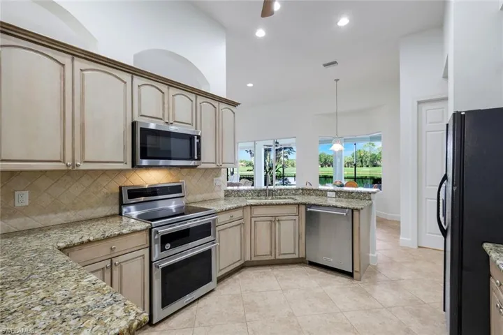 Kitchen featuring light-toned cabinetry, granite countertops, tile backsplash, and stainless steel appliances