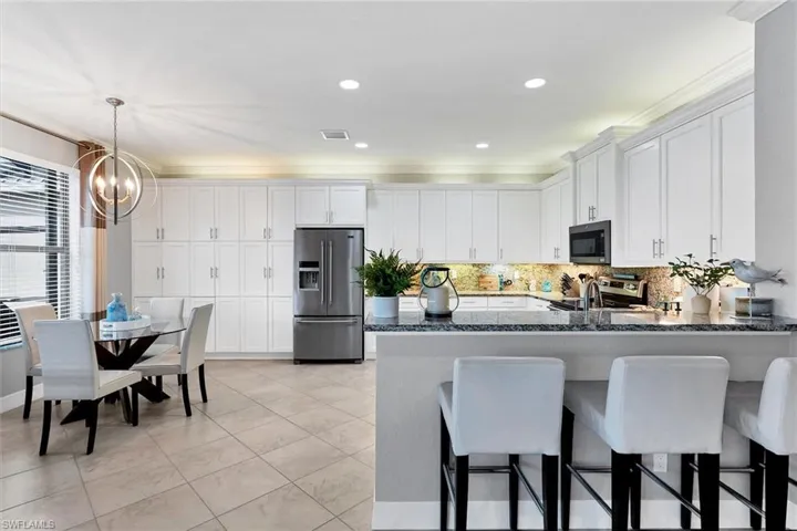 Kitchen featuring dark stone countertops, stainless steel appliances, kitchen peninsula, decorative light fixtures, and backsplash