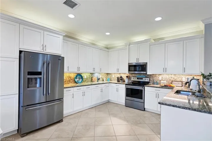 Kitchen with backsplash, dark stone countertops, appliances with stainless steel finishes, sink, and light tile floors