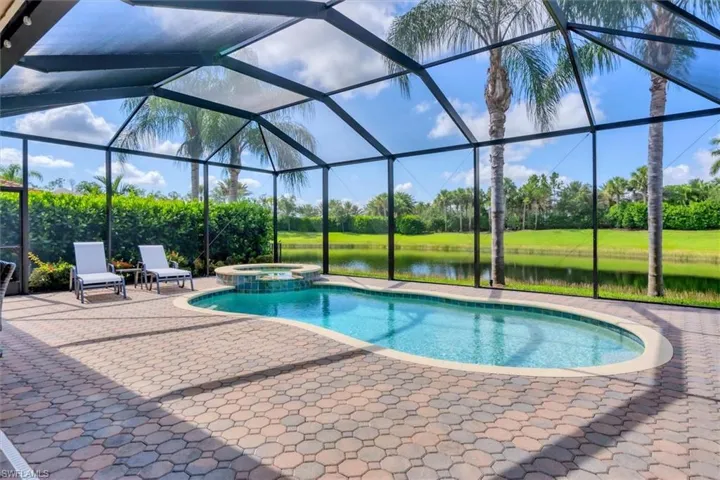 View of swimming pool with a patio area, glass enclosure, an in ground hot tub, and a water view
