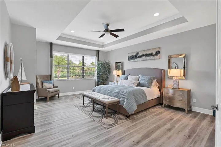 Bedroom with a tray ceiling, light wood-type flooring, and ceiling fan