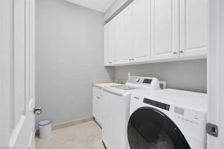 Laundry area featuring washer and dryer, cabinets, sink, and light tile floors