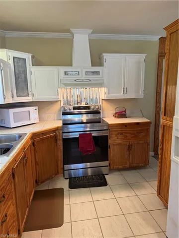Kitchen with stainless steel electric range, ornamental molding, wood finish cabinetry, range hood, and white cabinetry