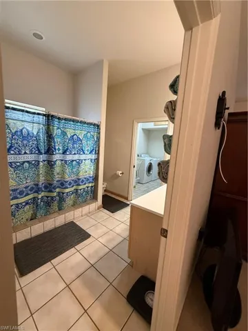 Full bath with vanity, curtained shower, independent washer and dryer, and light tile patterned floors