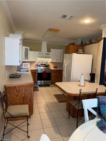 Kitchen with a kitchen breakfast bar, stainless steel appliances, tile countertops, wood finish cabinetry, and crown molding