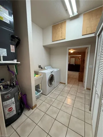 Laundry room featuring heating unit, water heater, washing machine and clothes dryer, light tile patterned floors, and a textured ceiling
