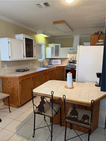 Kitchen featuring a breakfast bar area, range, a textured ceiling, white cabinetry, and refrigerator