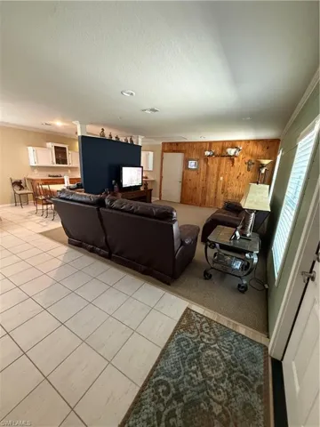 Living area with wooden walls, a textured ceiling, light tile patterned floors, ornamental molding, and light colored carpet