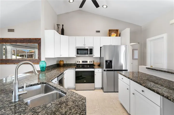 Kitchen with stainless steel appliances, dark stone counters, white cabinetry, ceiling fan, and vaulted ceiling