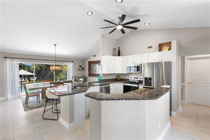 Kitchen with a peninsula, dark stone countertops, stainless steel appliances, a kitchen breakfast bar, and lofted ceiling