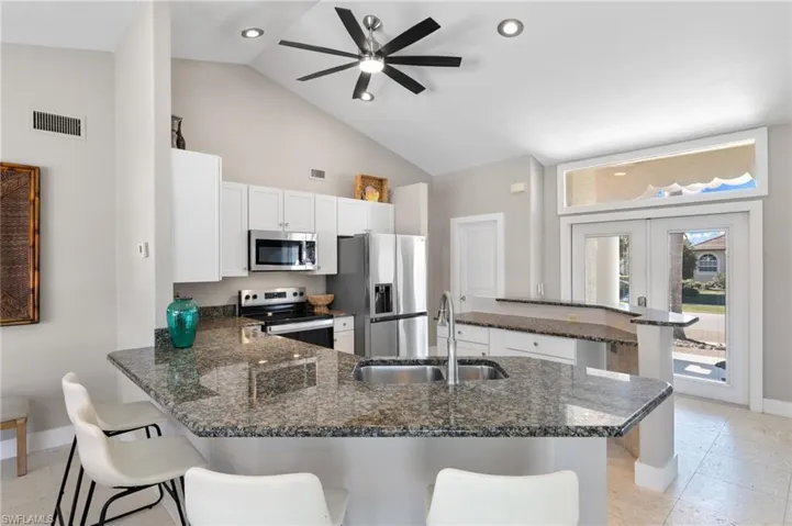 Kitchen with a peninsula, dark stone counters, a ceiling fan, stainless steel appliances, and a kitchen bar