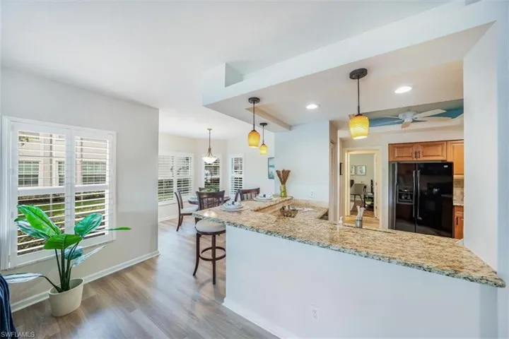 Kitchen featuring hanging light fixtures, light hardwood / wood-style flooring, light stone counters, black refrigerator with ice dispenser, and ceiling fan