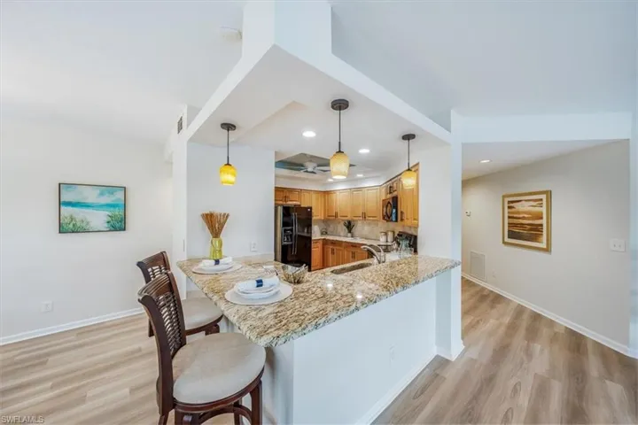 Kitchen with light hardwood / wood-style floors, light stone countertops, hanging light fixtures, black appliances, and backsplash
