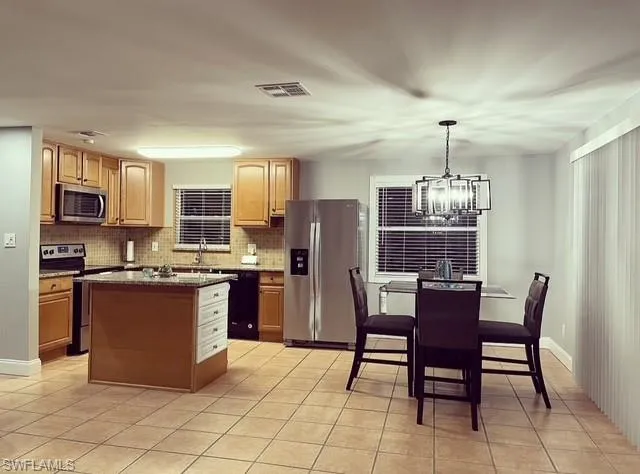 Kitchen with stainless steel appliances, dark stone countertops, a chandelier, wood finish cabinetry, and a kitchen island