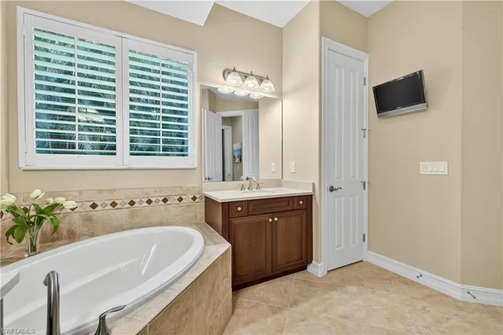 Full Primary Bathroom Ensuite with Soaking Tub, Plantation Shutters, and Linen Closet, and Mounted TV.