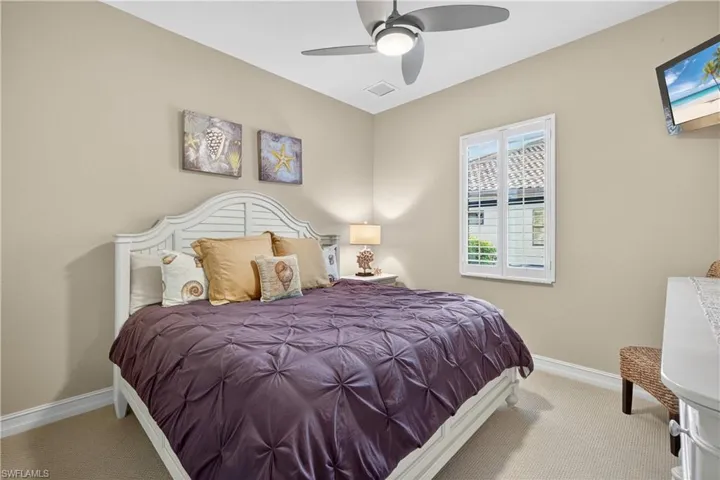 Carpeted 3rd Guest Bedroom Featuring High Baseboards, King Size Bed, Ceiling Fan, Mounted TV, and Plantation Shutters