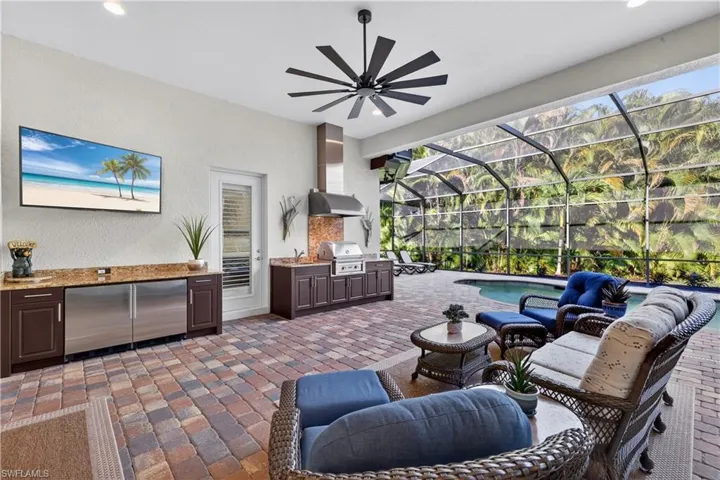 View of Lanai Featuring the Outdoor Kitchen with Polymer Never Fade Cabinets, Lynx Professional Grill, Dual Wine Coolers, Granite Counters, Upgraded Ceiling Fan, and Private Primary Bedroom Entry with Plantation shutters