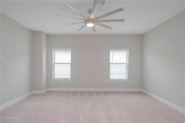 Unfurnished room with ceiling fan, light colored carpet, and a healthy amount of sunlight
