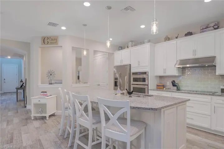 Kitchen with pendant lighting, a center island with sink, decorative backsplash, light wood-type flooring, and stainless steel appliances