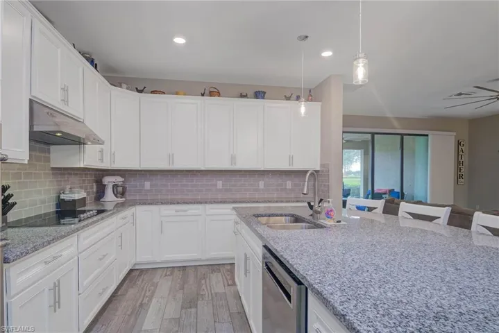 Kitchen featuring white cabinetry, dishwasher, sink, a kitchen bar, and black electric stovetop