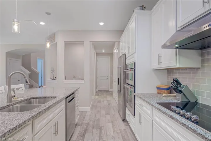 Kitchen with sink, light stone counters, decorative backsplash, white cabinets, and appliances with stainless steel finishes