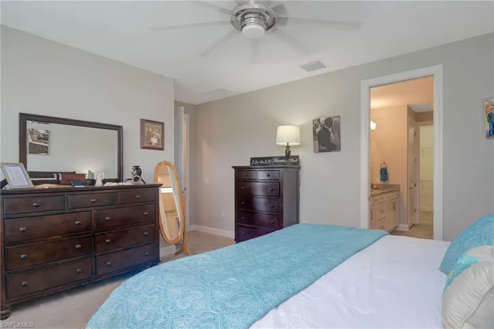 Bedroom featuring ceiling fan, light colored carpet, and ensuite bathroom