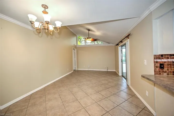 Unfurnished dining area featuring vaulted ceiling, ornamental molding, light tile floors, and ceiling fan with notable chandelier