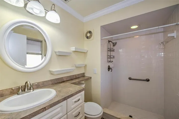 Bathroom with a tile shower, ornamental molding, vanity, and toilet