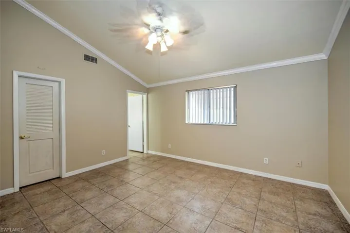Empty room featuring ornamental molding, ceiling fan, light tile flooring, and lofted ceiling