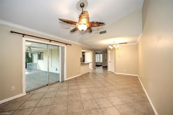 Tiled spare room with plenty of natural light, ceiling fan with notable chandelier, vaulted ceiling, and crown molding