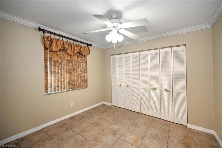 Unfurnished bedroom featuring ornamental molding, a closet, light tile flooring, and ceiling fan